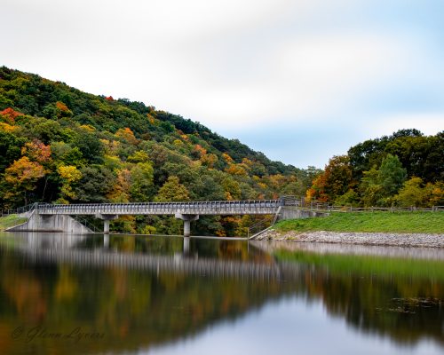 Steel truss bridge over a lake framed by autumn hills
