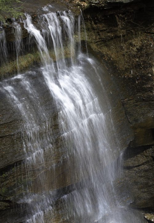 Waterfall cascading over layered rock ledges in a shaded gorge