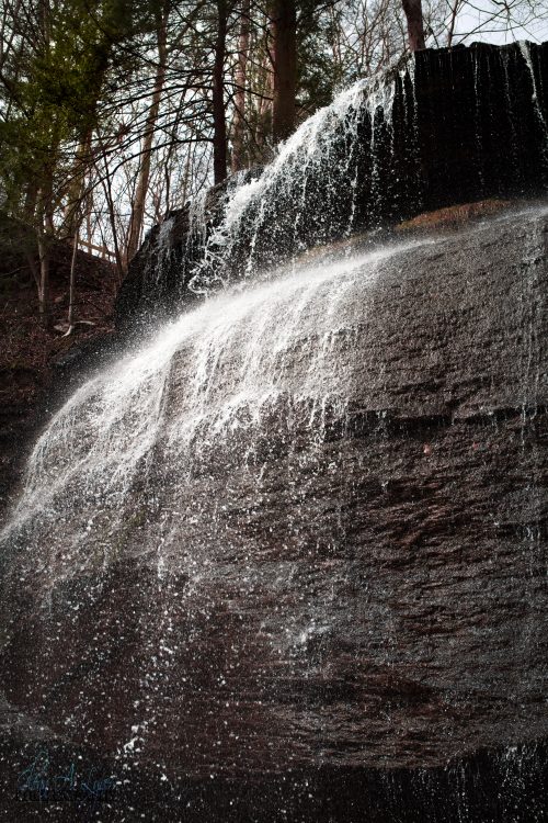 Waterfall spraying over a dark rock ledge in a forest