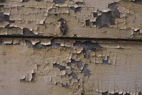 Peeling tan paint over weathered wood siding