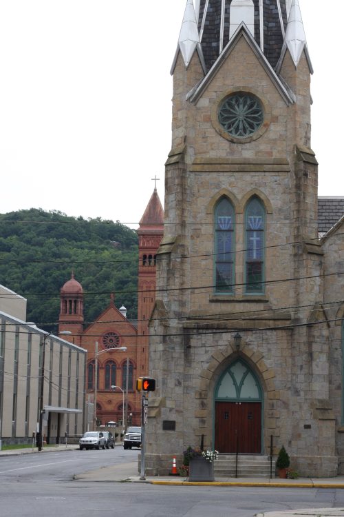 Stone church tower with rose window and red steeple in the distance