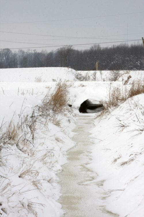 Frozen drainage ditch running through a snowy field