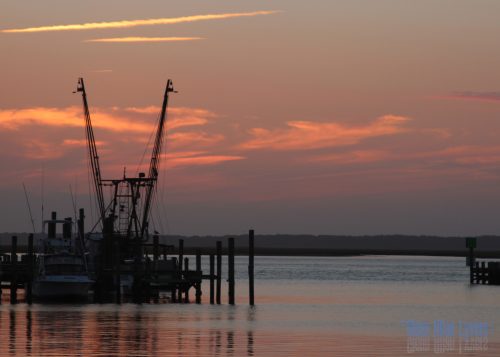 Fishing boats at a dock silhouetted against an orange sunset