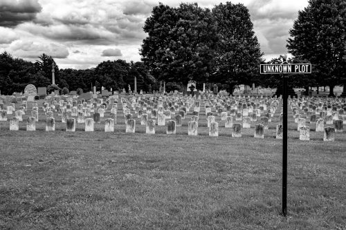 Rows of headstones beside an Unknown Plot sign in a cemetery