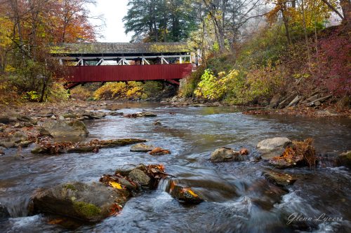 Red covered bridge over a rocky rushing creek in autumn