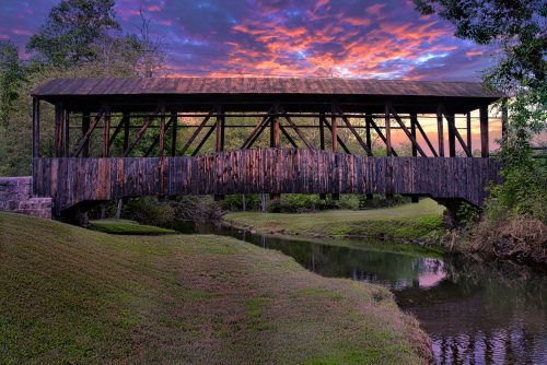 Covered bridge over a creek under a vivid sunset sky