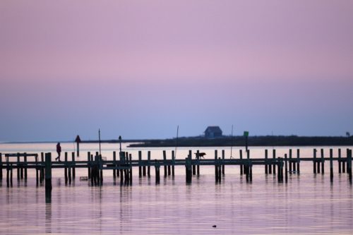 Silhouetted pier pilings on calm water under a pink sunset sky